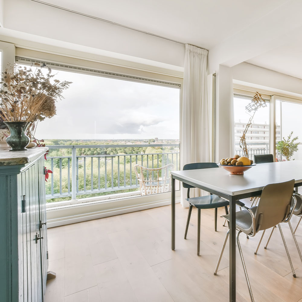 A modern flat showing a dining table and large windows showing outside 
